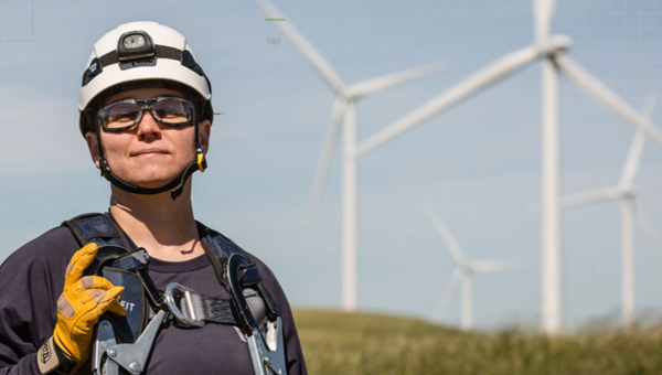 Employee in hard hat with wind turbines in distance