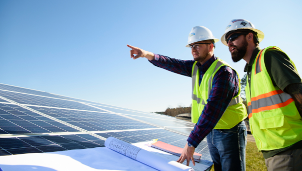 Employees in hard hats next to solar panel