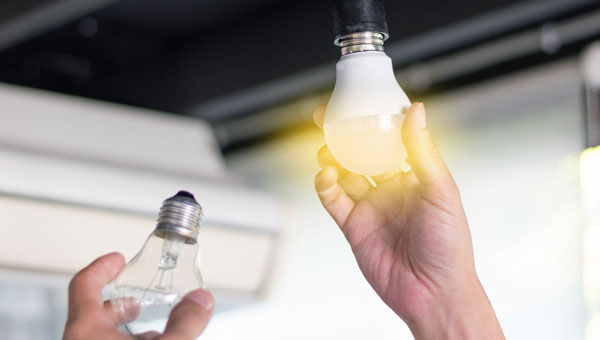 Hands changing out a regular lightbulb to a energy efficient lightbulb
