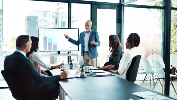 People sitting on chairs in an office with glass walls and a man giving a presentation