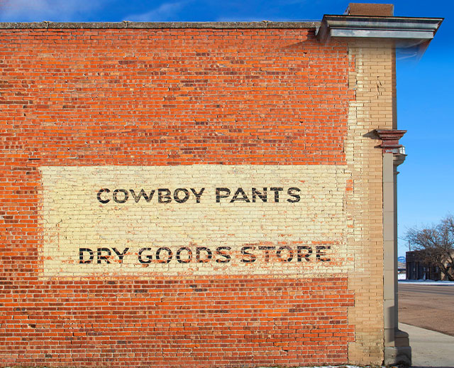 Sign on a brick store that reads "Cowboy Pants Dry Goods Store"