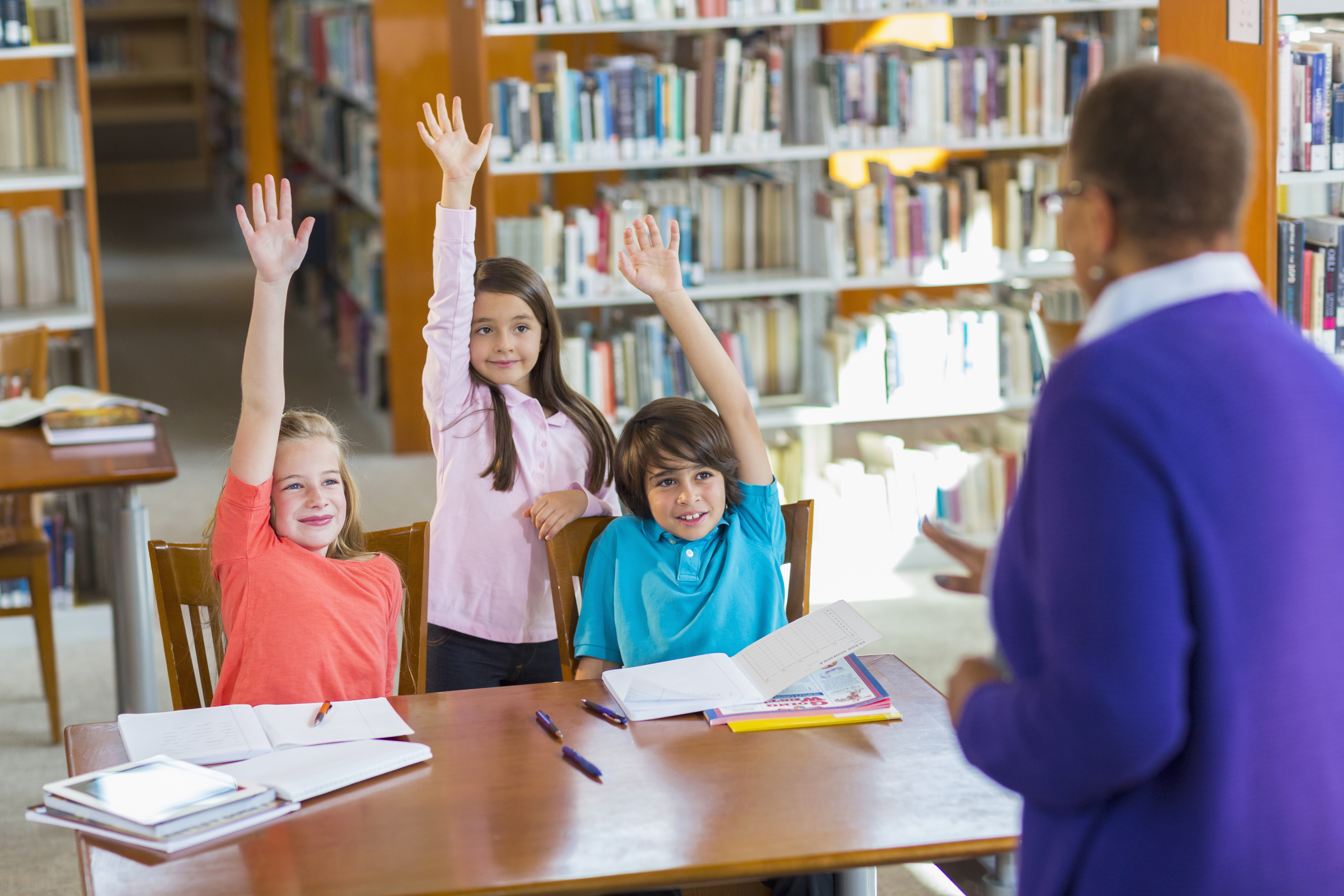 Students raising their hands in a library Students raising their hands in a library