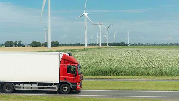 Tractor trailer driving across field with wind turbines in background