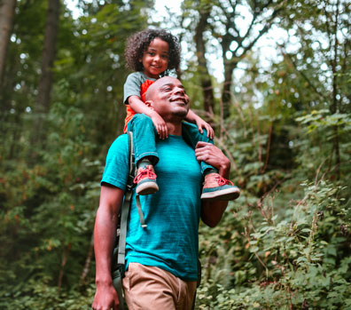 A father walking in the woods with his son sitting on his shoulders
