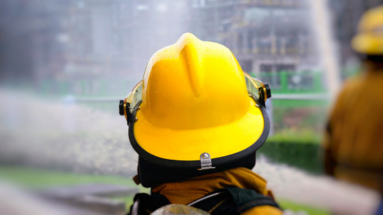 Firefighter in yellow helmet amid water spray during emergency scene.