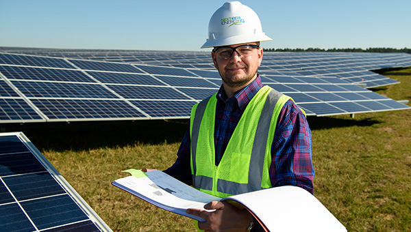 NextEra Energy Resources employee in a hard hat holding paperwork with solar panels in the background