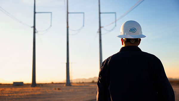 NextEra Energy employee in front of transmission lines with hard hat
