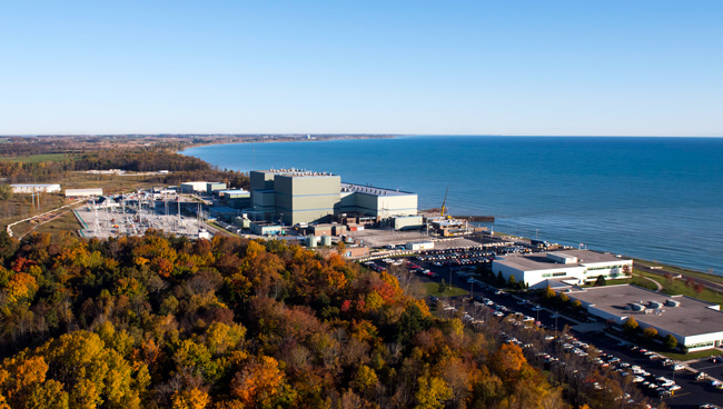 Aerial view of Point Beach Nuclear Plant situated along the western shore of Lake Michigan, surrounded by autumn foliage under a clear blue sky.