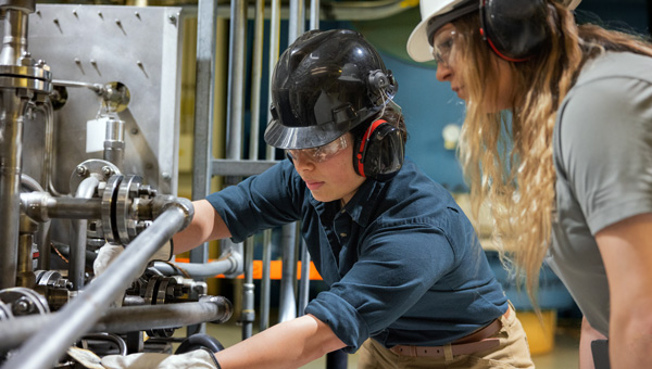 Nuclear plant workers inspect piping and valves with protective gear at Point Beach facility.
