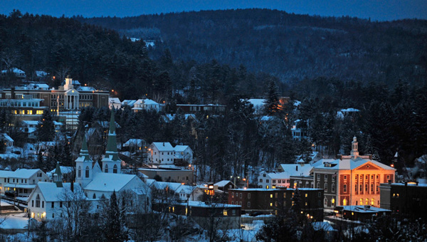 New England winter town at dusk with snow, churches, and glowing hillside architecture.